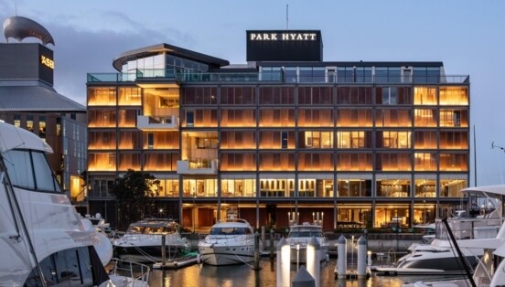 Das warme Licht des Park Hyatt Hotels spiegelt sich im Hafenbecken von Auckland, während die weißen Yachten direkt davor vor Anker liegen.