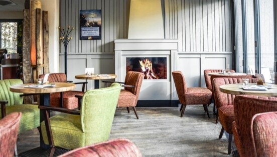 Gemütlicher Gastraum des ALEX in Wiesbaden mit loderndem Gaskamin, runden kleinen Tischen und bequemen Sesseln in Grün und Rot.