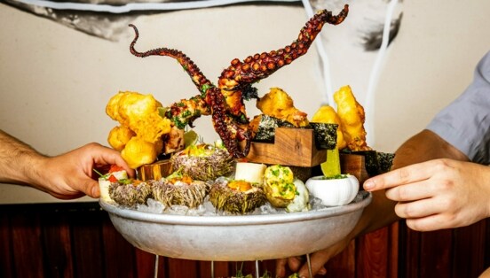 Hände drapieren auf einer tiefen Platte mit Eis diverse Speisen – von Tintenfisch über Frittiertes bis Kaviar.