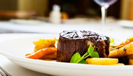 Gegrilltes Rinderfilet auf weißem Teller mit gebratenen Karotten und grünen Erbsensprossen.