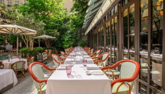 Begrünter Innenhof eines eleganten Restaurants mit gedeckten Tischen und Sonnenschirmen.