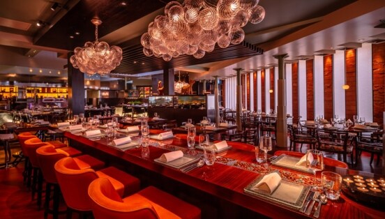 Opulent eingerichteter Speisesaal mit eingedeckter Holztafel und offener Küche.