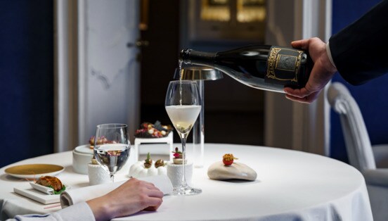 In einem Restaurant mit tiefblauen Wänden schenkt ein Kellner edlen Schaumwein in ein Glas ein.