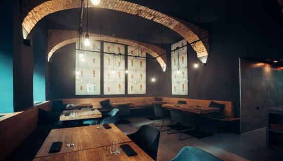 Moderner Speisesaal mit eingedeckten Holztischen und dunklen Wänden mit Gewölbedecke.