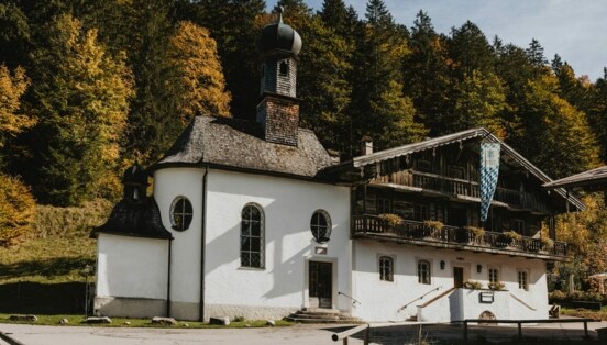 Traditionelles, bayerisches Gasthaus mit Kapelle vor einem Waldgebiet.