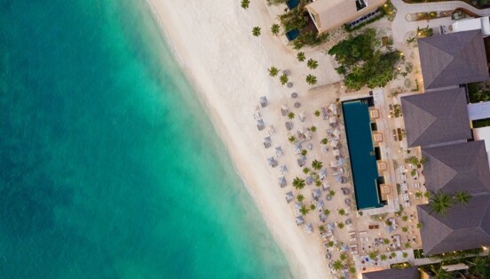 Hotelresort mit Pool und Sanstrand am türkisblauen Meer aus der Vogelperspektive.