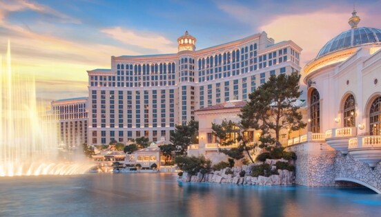 Prunkvoller Hotelkomplex hinter einem künstlichem See mit beleuchteter Wasserfontäne bei Sonnenuntergang.