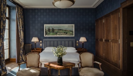 Gemütliches Hotelzimmer mit Doppelbett vor dunkelblauer Tapete und großem Holzkleiderschrank.