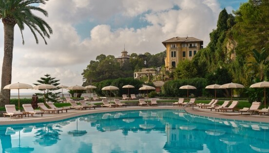 Luxuriöse Hotelterrasse mit Pool und Liegestühlen an einer mediterranen Küste.