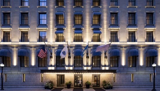 Beleuchtete Fassade eines Luxushotels mit wehenden Fahnen über dem Eingangsbereich.