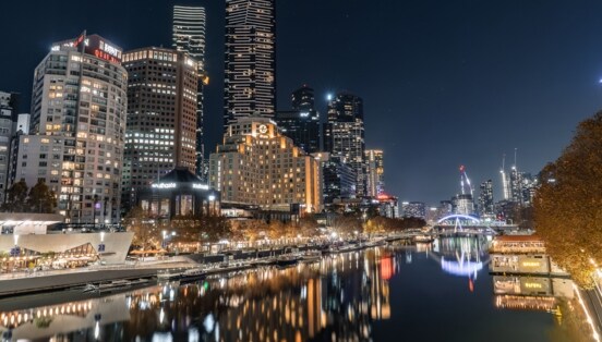 Beleuchtete Skyline mit Hochhäusern an einem Flussufer bei Nacht.