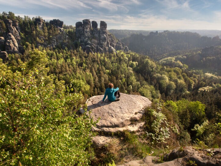 Eine Frau auf einer Felsenplattform, die auf die Sächsische Schweiz blickt