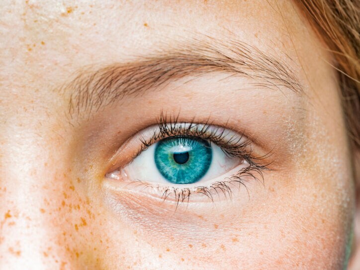 Nahaufnahme eines blauen Augens einer Frau mit Sommersprossen