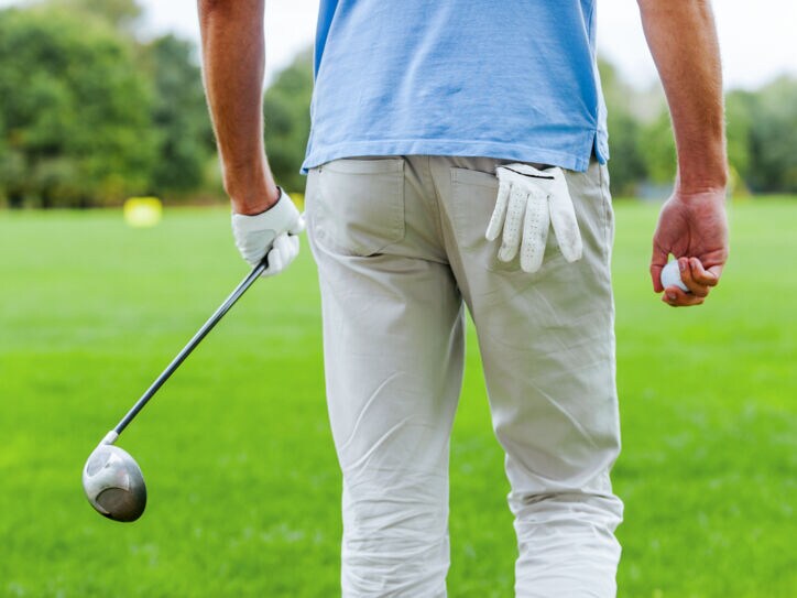 Rückansicht eines männlichen Golfspielers, der mit Golfball und Driver in der Hand weggeht