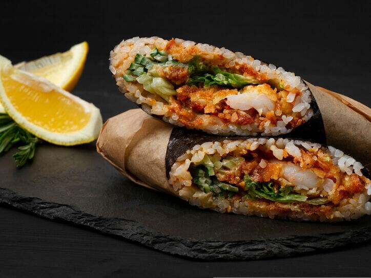 Zwei große Reisrollen mit Gemüse und Garnele auf schwarzer Schieferplatte angerichtet