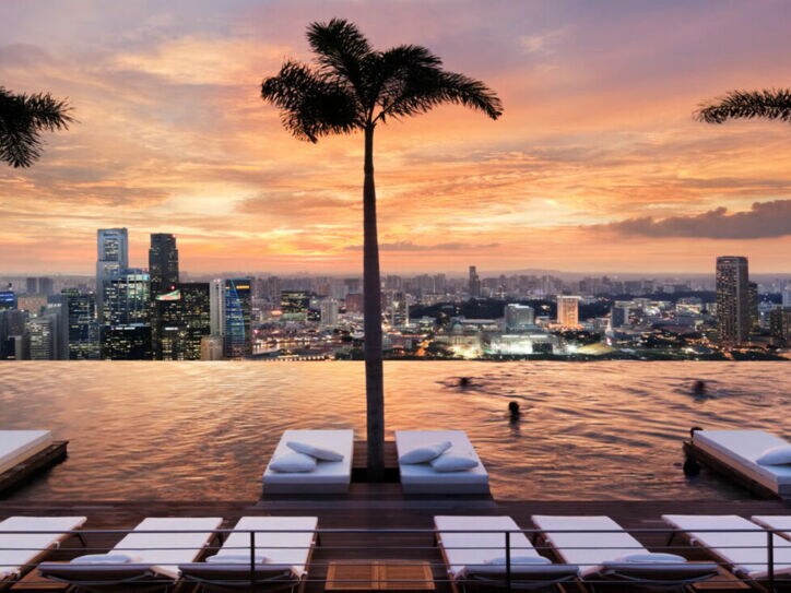 Ein endlos scheinender Pool mit Blick auf die Skyline Singapurs, mit Liegen und Palmen im Wasser
