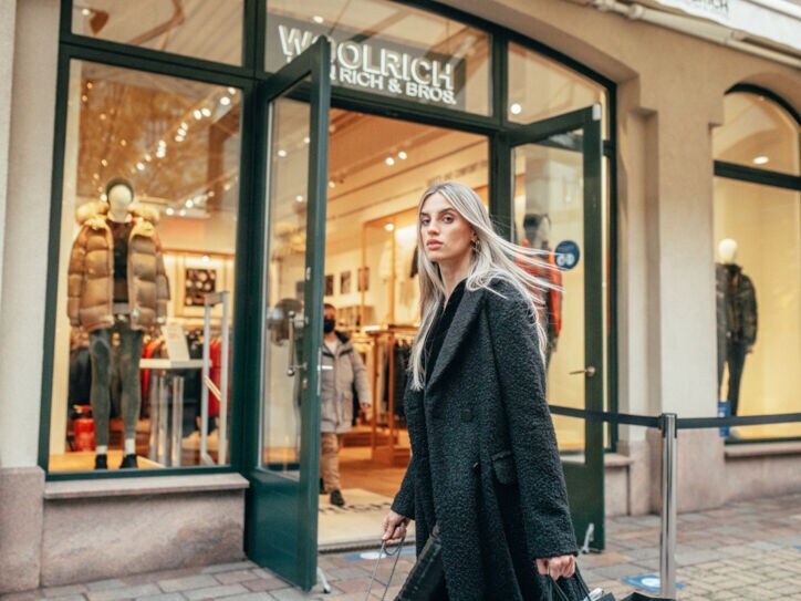 Eine Frau in langem schwarzen Mantel läuft an einem winterlichen Schaufenster vorbei