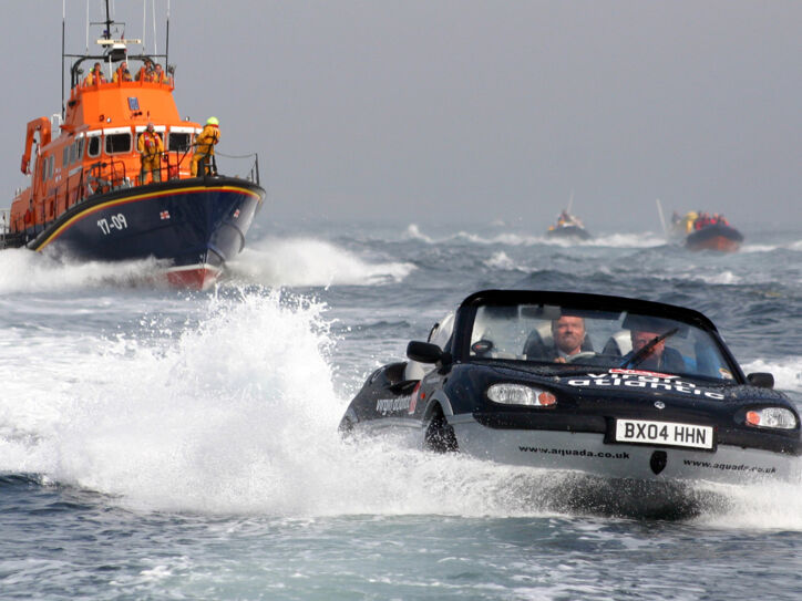 Ein Amphibienfahrzeug fährt auf dem Wasser zwischen mehreren Schiffen