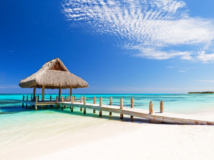 Ein weißer Sandstrand mit Steg und Pavillon am türkisfarbenen Meer in der Dom Rep