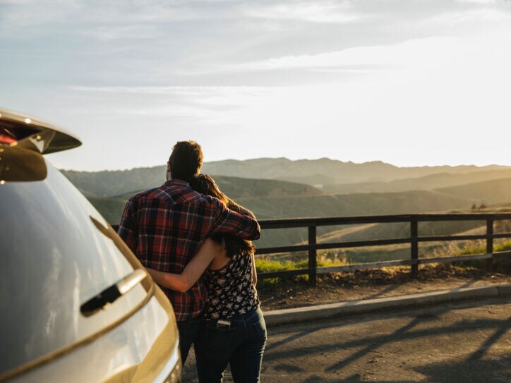 Ein Paar steht vor dem Auto und genießt die Aussicht über die Landschaft.