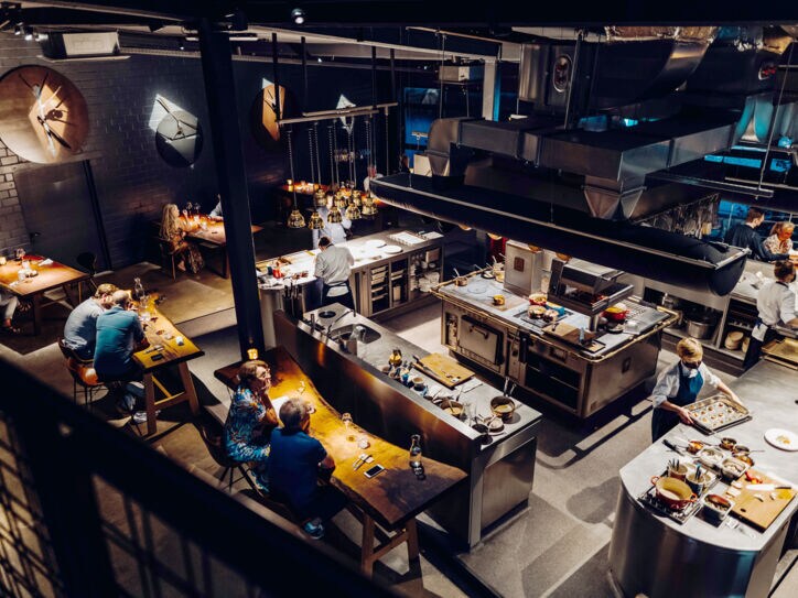 Blick in ein Restaurant mit Holztischen und mittiger Kücheninsel