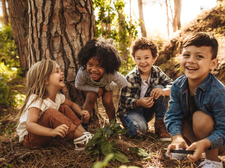 Vier fröhliche Kinder sitzen vor einem Baum im Grünen