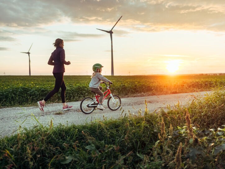 Eine joggende Frau ist mit einem kleinen Mädchen auf dem Fahrrad bei Sonnenuntergang unterwegs