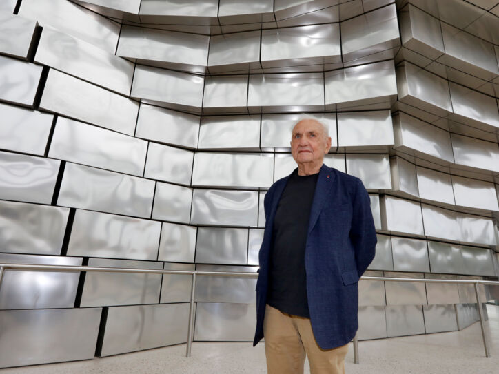 Architekt Frank Gehry vor einer Fassade aus glänzenden Aluminiumplatten