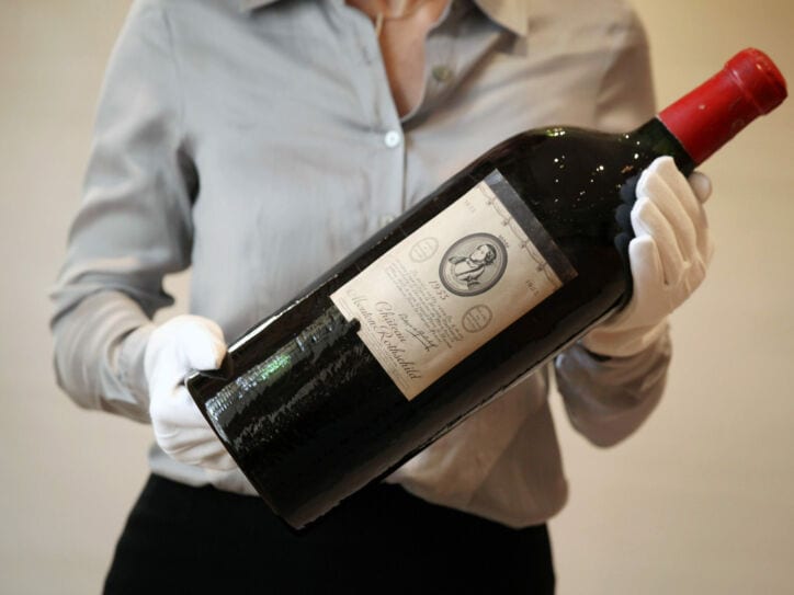 Eine große Flasche Rotwein der Marke Chateau Mouton Rothschild wir von einer Person mit weißen Handschuhen gehalten