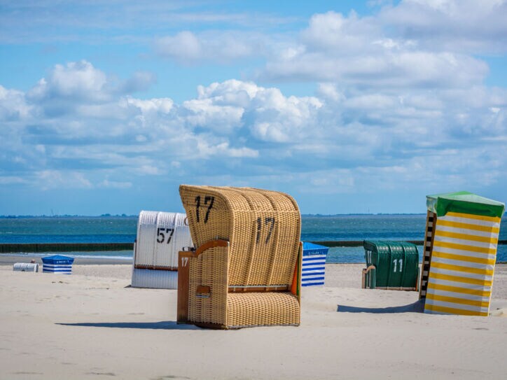 Strandkörbe an einem menschenleeren Sandstrand vor blauem Himmel