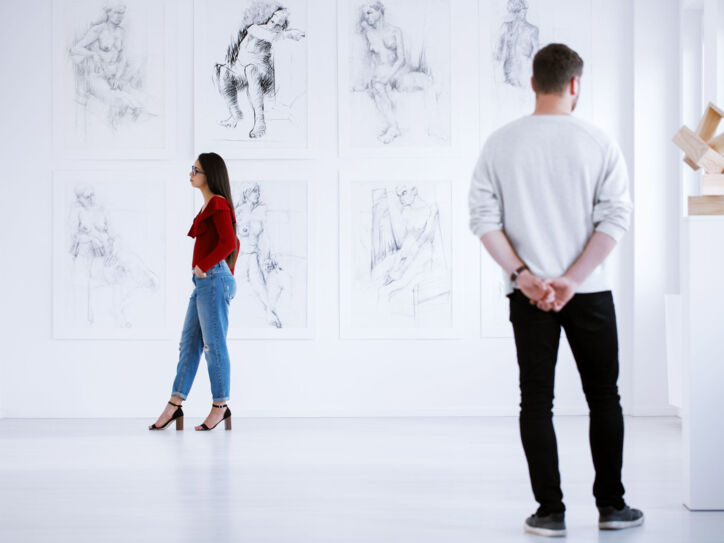 Zwei Personen schauen sich in einem weißen Ausstellungsraum Zeichnungen und Skulpturen an
