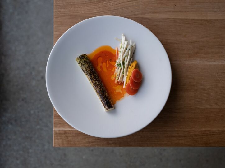 Weißer Teller mit Karotten in Soße auf einem braunen Holztisch