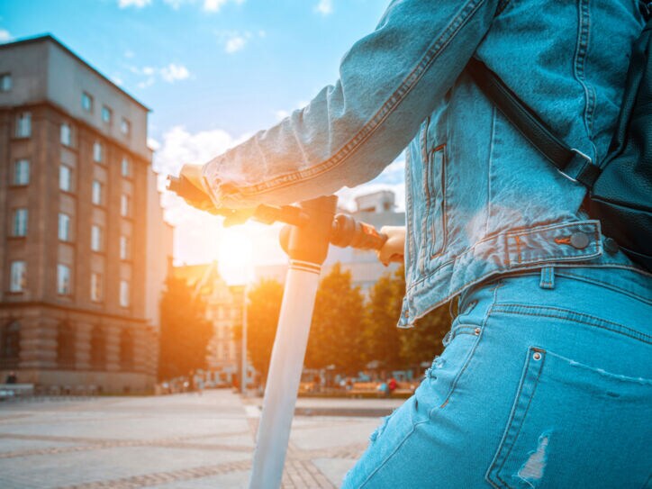 Eine Person in Jeanskleidung von hinten auf einem E-Tretroller auf einer Straße