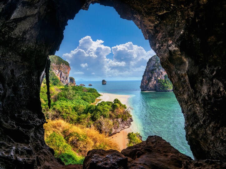 Blick aus einer Höhle auf Strand, Meer und Bäume