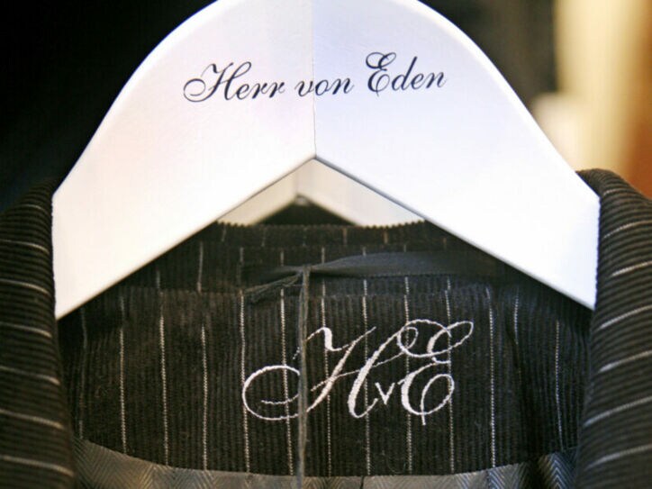 Detailaufnahme eines Nadelstreifenanzugs auf einem weißen Kleiderbügel mit einer geschnörkelten Aufschrift