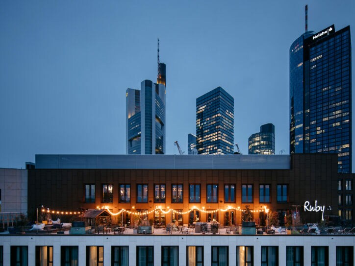 Eine beleuchtete Rooftop-Bar vor der Frankfurter Skyline bei Nacht
