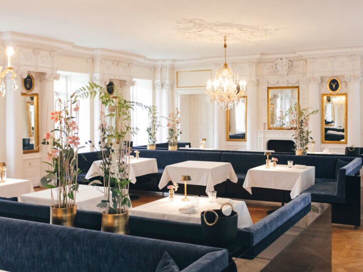 Innenaufnahme eines edlen Restaurants mit Kronleuchtern und gedeckten Tischen an blauen Samtbänken