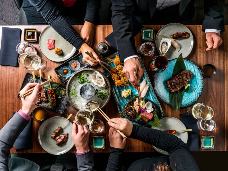 Hände nehmen mit Stäbchen Essen von Tellern in der Mitte eines Tisches
