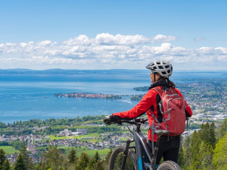 Rückansicht einer Frau mit einem Fahrrad vor dem Panorama des Bodensees
