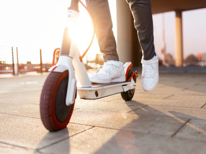 Nachaufnahme eines Rollers, auf dem ein Mann mit weißen Turnschuhen steht, Symbolbild