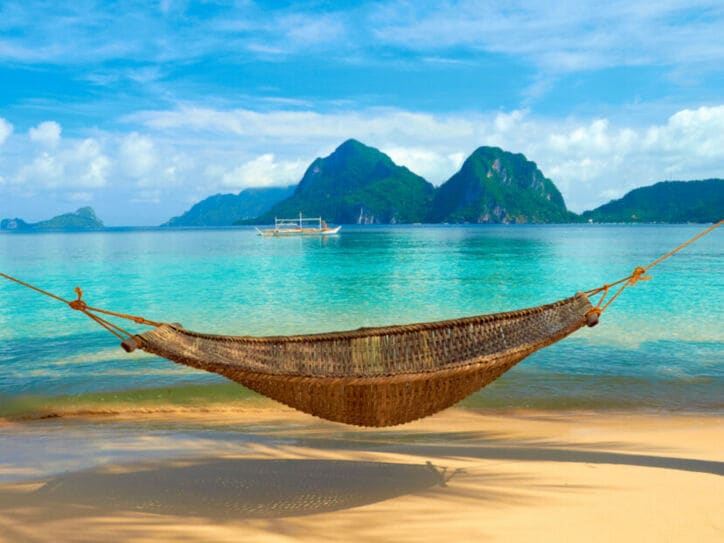 Eine Hängematte ist an einem Sandstrand vor türkisblauem Meer aufgespannt