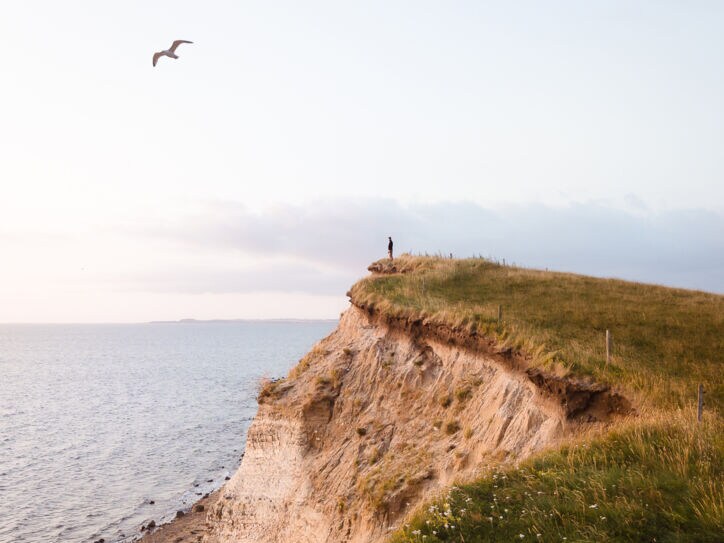 Eine Person steht auf einer Klippe und blickt aufs Meer