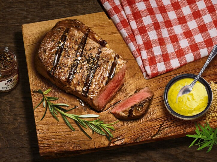 Aufsicht eines gebratenen, angeschnittenen Steaks auf einem Brett neben einer Schale mit Senf.