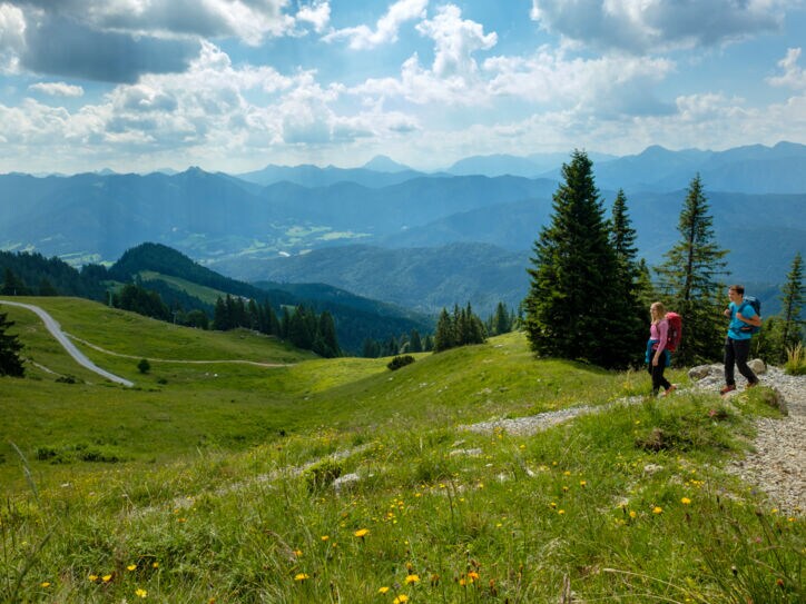 Ein wanderndes Paar mit Rucksäcken auf einem Weg inmitten einer grünen Berglandschaft.