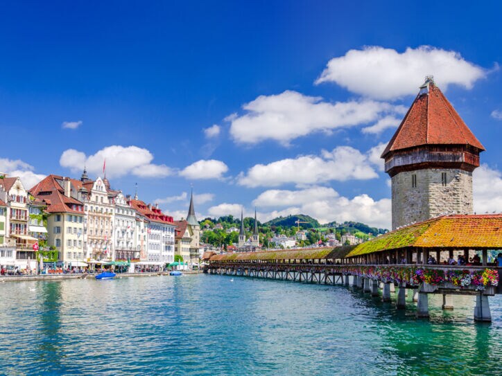 Altstadtpanorama von Luzern am Wasser mit einer hölzernen Brücke vor einem Wasserturm.
