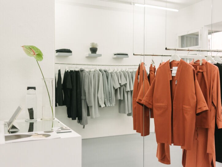 Puristische, elegante Kleidungsstücke, nach Farben sortiert, auf hängenden Kleiderstangen in einer Boutique.