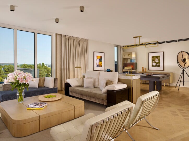 Eine modern und mit hellem Mobiliar eingerichtete Hotel-Suite mit großer Fensterfront.