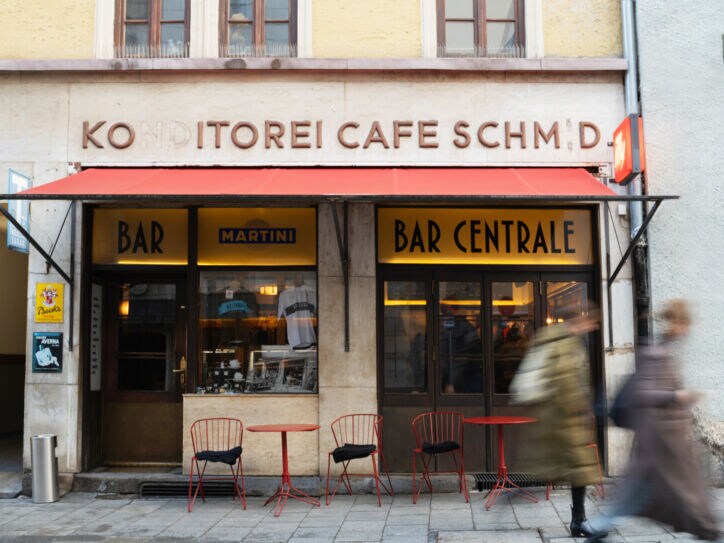 Außenansicht der Bar Centrale mit roter Markise sowie Bistrotischen und Stühlen.