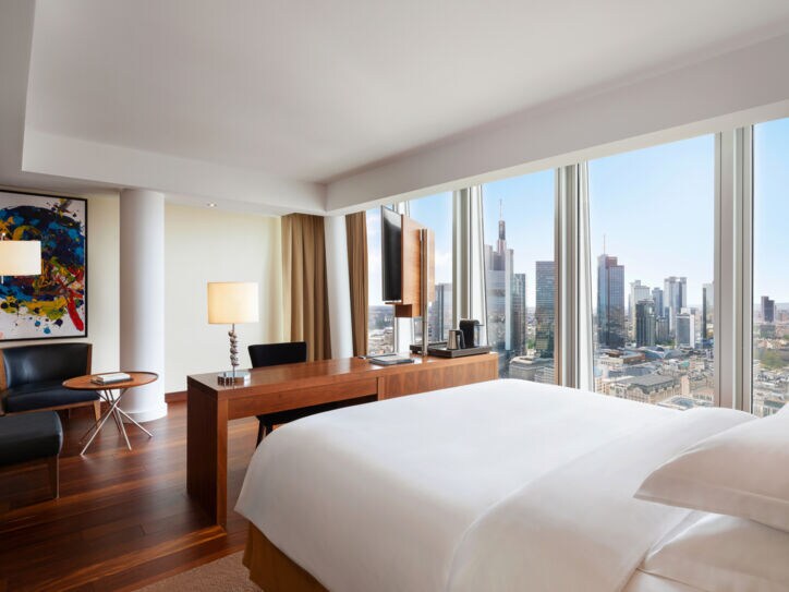 Modernes Hotelzimmer mit Blick auf die Frankfurter Skyline durch bodentiefe Panoramafenster.