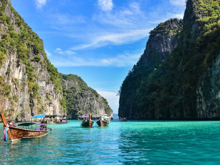 Boote in einer Lagune im türkisblauen Meer mit grün bewachsenen Felsen im Hintergrund. 